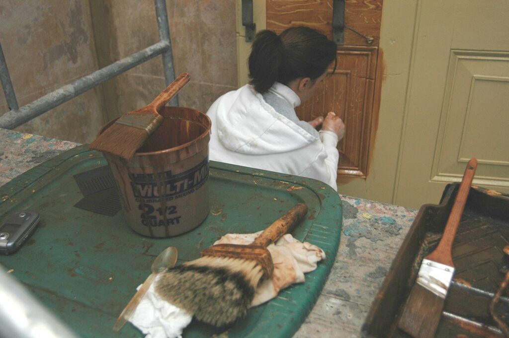 A skilled artisan adding a faux wood grain finish to some of the full-length exterior shutters.